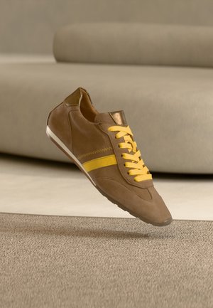 Brauner Wildleder-Sneaker mit gelben Schnürsenkeln und Streifen, versehen mit einem metallisch goldenen Fersenakzent und einem glatten, schlanken Design.
