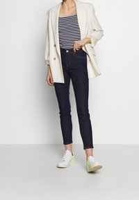 Bílý dvouřadý blazer, pruhovaná námořnická modrá a bílá tílko, tmavé skinny džíny a bílé tenisky s neonovými akcenty.