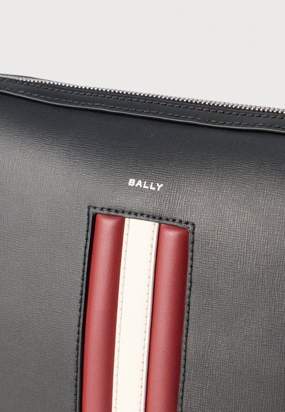 Μαύρη δερμάτινη θήκη με υφή, με ασημένιο φερμουάρ, που διαθέτει κάθετη κόκκινη και λευκή δερμάτινη ρίγα και το λογότυπο "BALLY" πάνω.