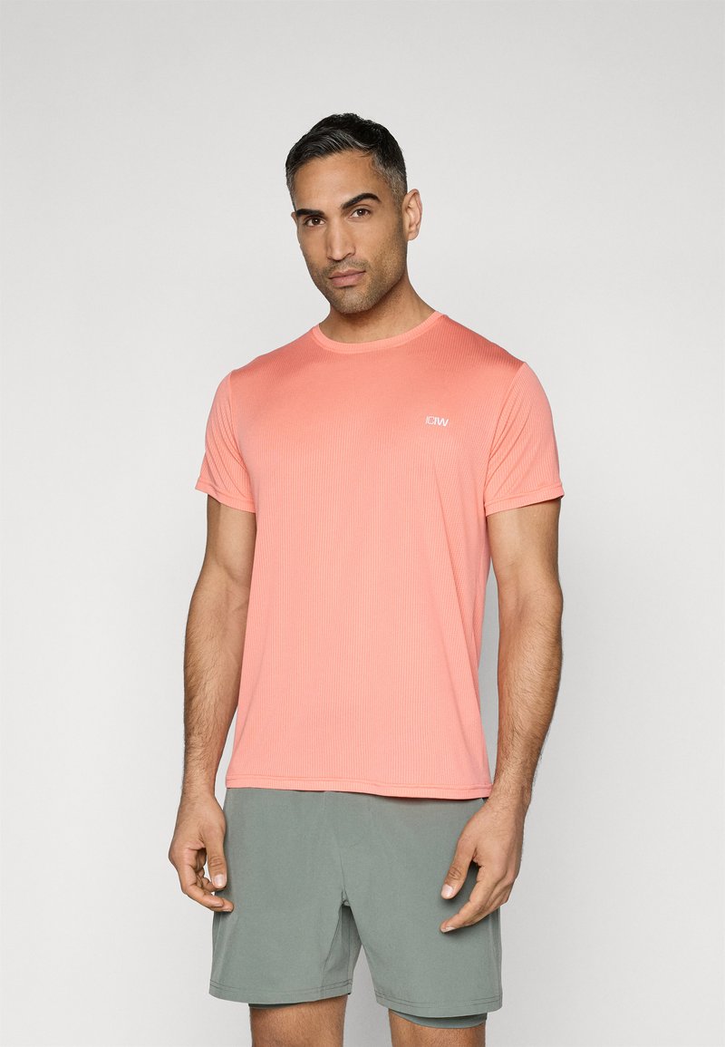 Tricou sportiv scurt din coral, cu mâneci scurte, textură canelată, guler rotund și detaliu logo pe piept, asociat cu pantaloni scurți de culoare verde deschis.