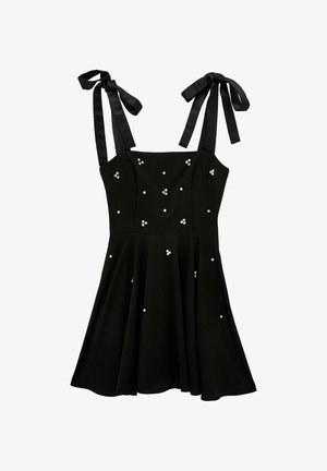 Robe noire sans manches avec bretelles nouées aux épaules, corsage ajusté, jupe évasée et petites perles blanches dispersées en embellissements.