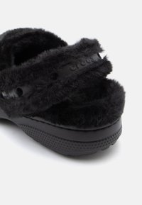 Μαύρα Crocs με πλούσια γούνινη επένδυση, που διαθέτουν φαρδιές λωρίδες, μικρές κυκλικές τρύπες αερισμού και υφή στη σόλα.