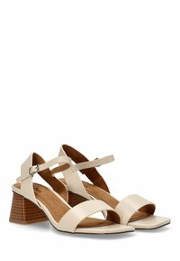 Sandalias de cuero beige con tacón cuadrado, que cuentan con dos correas cruzadas anchas y una correa ajustable en el tobillo. Interior suave para mayor comodidad.