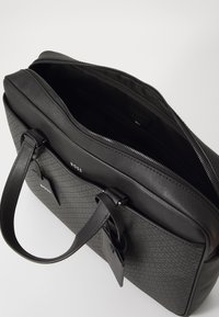 Sort forretningsmappe med glat og tekstureret læder, lynlåslukning, dobbelthåndtag og et subtilt mønsterdesign på fronten. Indvendige rum er synlige.