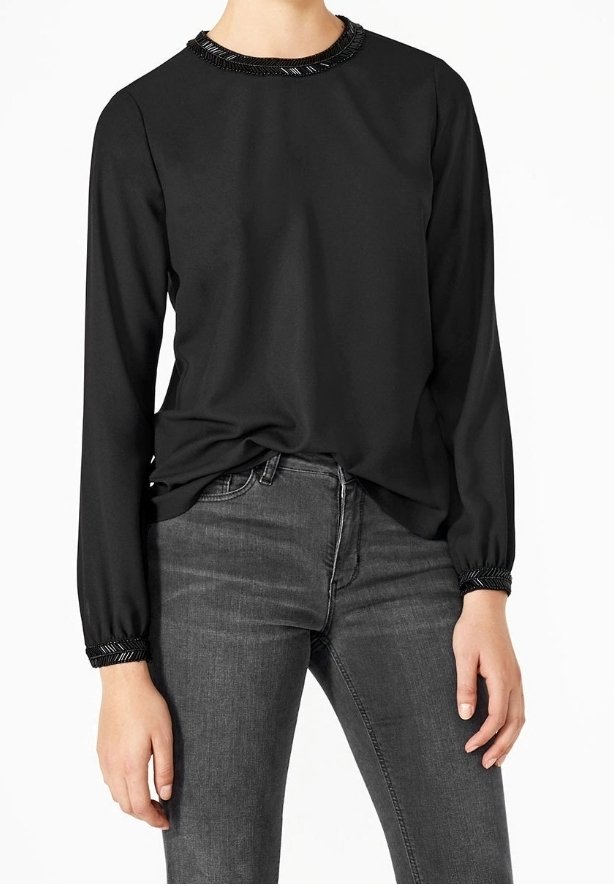 Top nero a maniche lunghe con collo decorato con perline e polsini arricciati, abbinato a jeans aderenti grigio scuro. Tessuto di stoffa liscio.