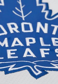 Tessuto blu con testo ricamato bianco "TORONTO MAPLE LEAFS" e un design stilizzato della foglia d'acero. Il testo ha una finitura testurizzata.