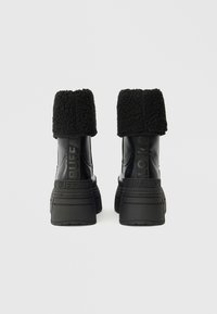 Botas de tornozelo pretas com um punho de fleece texturizado e sola em borracha. Apresentam uma marcação em relevo e um design elegante. Sola plana e construção resistente.