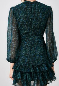 Mörk blomstrig klänning med genomskinliga ärmar, volangkant och figursydd midja. Färgerna inkluderar djupgrön och blå med texturerad design.