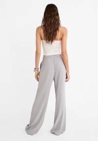 Vaaleanharmaat, leveälahkeiset housut, jotka on valmistettu pehmeästä kankaasta, jossa on joustava vyötärö ja sivutaskut, yhdistetty tiukkaan valkoiseen hihattomaan toppiin.