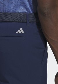 Tamsiai mėlynos sportinės kelnės su austu liemeniu, šonine kišene ir subtiliu baltu logotipu ant galinės kišenės. Lygus audinys ir pritaikyta fit.