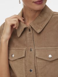 Jachetă cămașă maro din catifea cu guler ascuțit, nasturi capse și buzunare la piept; prezintă o textură striată și accesorii argintii.