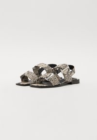 Flat sandals featuring a snake print pattern in beige and black, with wide cross straps, silver hardware accents, and a smooth sole.
