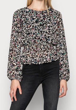 Bluzka w kwiatowy wzór z długim rękawem i marszczonym pasem, zestawiona z czarnymi dopasowanymi dżinsami, noszona przez stojącą osobę na jednolitym tle.