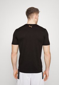 Camiseta negra de manga corta con cuello redondo y un pequeño logo naranja de Puma en la parte superior de la espalda, fabricada en un material liviano.