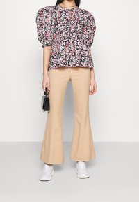 Blusa negra de flores con mangas abullonadas y dobladillo con volantes, combinada con pantalones beige de campana y zapatillas blancas. Un bolso negro añade contraste.