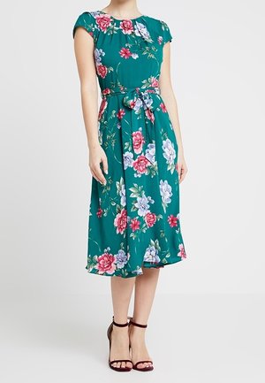 Abito floreale in tessuto teal, lungo fino al ginocchio con maniche a cappuccio, dotato di una cintura annodata in vita e caratterizzato da modelli floreali colorati in rosa e blu.