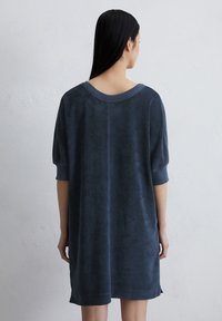 Marineblauwe oversized jurk met een zachte, gestructureerde stof, brede halslijn en korte mouwen, met een relaxte pasvorm en zijsplitten.
