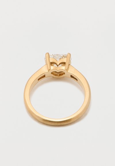 Kuldne sõrmus, millel on südamekujuline seade ja läbipaistev teemant. Sile rõngas läikiva viimistlusega ja kivi all avatud disain.