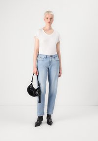 Licht gewassen rechte jeans met subtiele slijtage, gecombineerd met een aansluitend wit T-shirt en een gestructureerde zwarte handtas. Zwarte enkellaarsjes maken de look af.
