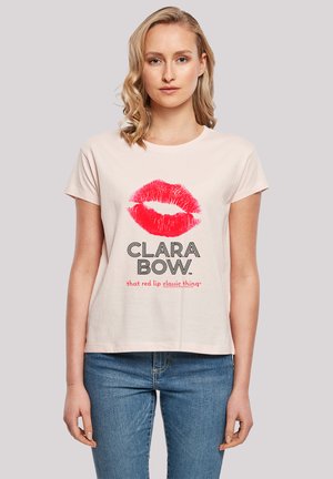 Light pink cotton t-shirt featuring a red lip print and text reading "CLARA BOW" in black, with a relaxed fit and short sleeves.