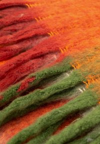 Wełniana tkanina w mieszanych odcieniach pomarańczowego, czerwonego i zielonego z wykończeniem w formie frędzli. Tekstura jest miękka i włóknista, z widocznymi włóknami.