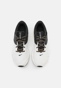Scarpe sportive bianche con tomaia in mesh testurizzato, accenti neri e lacci decorativi. Presentano un collare imbottito e un logo sulla linguetta.