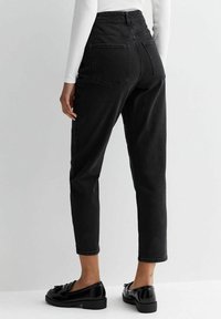 Svarta högmidjade jeans med avsmalnande ben och bakfickor, i kombination med blanka svarta loafers. Slät tyg med en lätt textur.