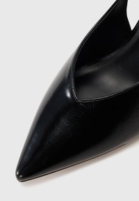 Scarpa nera con tacco alto a punta realizzata in pelle lucida, caratterizzata da un profondo taglio a V sui lati e una superficie liscia e strutturata.
