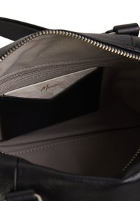 Interior de un bolso de mano de cuero negro con un forro beige. Cuenta con un bolsillo con cremallera y un compartimento para tarjetas de crédito con un patrón decorativo en su interior.