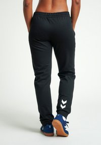 Svarta sweatpants med ett rynkat midjeband, sidofickor och vita chevronmönster på underbenet. Slät tyg, avslappnad passform.