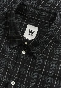 Black and white plaid button-up shirt with a structured collar, featuring white button closures and a textured fabric. Tag visible.