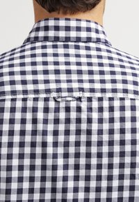Camicia a scacchi bianca e blu navy con colletto classico, cuciture in vista e dettaglio ad anello sul retro, realizzata in tessuto leggero.