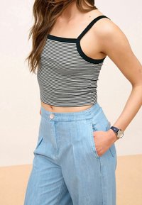 Stribet crop top med sorte og hvide vandrette striber, parret med lyseblå vide bukser med knapdetalje og sidelommer.
