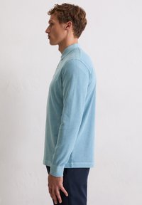 Lichtblauw poloshirt met lange mouwen en kraag, gemaakt van zachte stof. Heeft een rechte zoom en aansluitende manchetten.