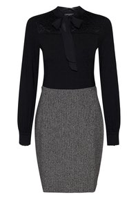 Top nero con dettagli in pizzo e fiocco al colletto, abbinato a una gonna a tubino texturizzata in bianco e nero. Maniche lunghe, design aderente.