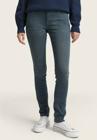 Sötétkék, skinny farmernadrág sima textúrával, enyhe elasztikussággal és hátsó zsebekkel, fehér sportcipőkkel, fekete csíkokkal párosítva.