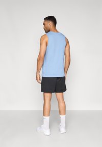 Φωτεινό γαλάζιο αμάνικο τοπ συνδυασμένο με μαύρο σορτς. Το μοντέλο φοράει λευκά αθλητικά παπούτσια και λευκές κάλτσες σε μέγεθος πλήρους μήκους.