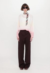 Pulover tricotat cu gradient, având un model în zigzag, asortat cu pantaloni largi, maro închis, cu un model în zigzag. Modelul poartă ochelari de soare negri, supradimensionați.