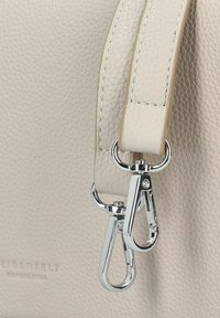 Bolso de mano de cuero de color beige claro con superficie texturizada, asas planas y herrajes plateados con ganchos de presión para sujeción.