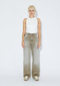 Top sin mangas blanco y jeans de pierna ancha gris claro con un ligero desvanecimiento, combinados con zapatillas ligeras. Diseño simple y colores neutros.