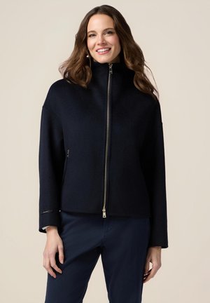 Chaqueta azul marino con cremallera, hecha de material suave, que cuenta con un alto cuello, mangas anchas y bolsillos laterales con detalles de hardware plateado.