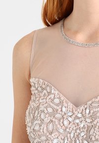 Rosa klänning med ett nätliv, dekorerad med paljetter och ädelsten-liknande accenter, med hög halsringning och intrikata detaljer.