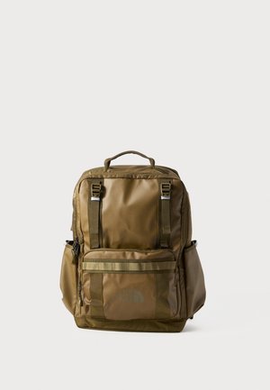 Sac à dos rectangulaire marron avec une poignée en haut, une poche zippée à l'avant, des poches latérales et deux sangles de fixation verticales sur un fond uni.