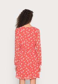 Vestido vermelho com mangas longas, estampa floral, cintura ajustada e decote nas costas. Leve, com uma textura suave e silhueta fluida.