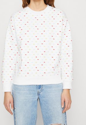 White sweatshirt with multicolored small rectangular patterns; features a round neckline, ribbed cuffs, and a relaxed fit. Paired with distressed denim.