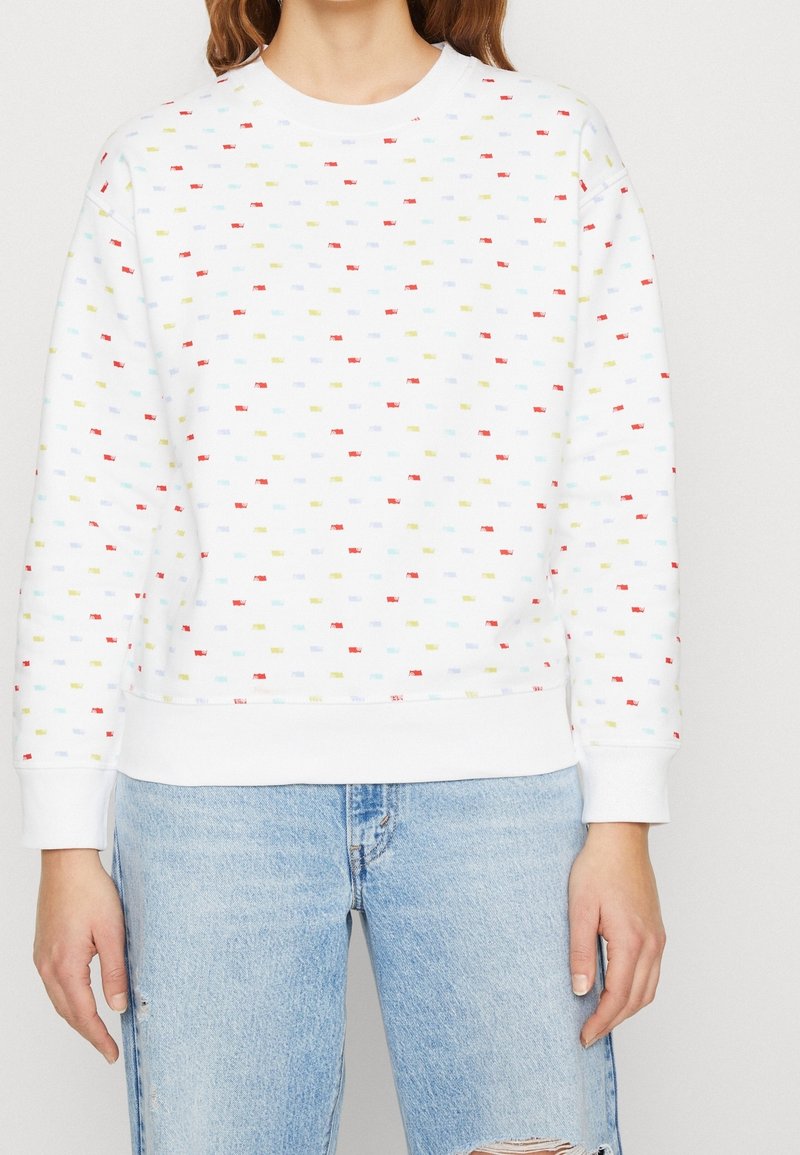 Felpa bianca con piccoli motivi rettangolari multicolori; presenta un colletto rotondo, polsini a costine e una vestibilità rilassata. Abbinata a jeans strappati.