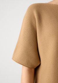 Bluză cu mâneci scurte, lejeră, dintr-un material tricotat de culoare bej deschis, cu un model texturat și decolteu larg.