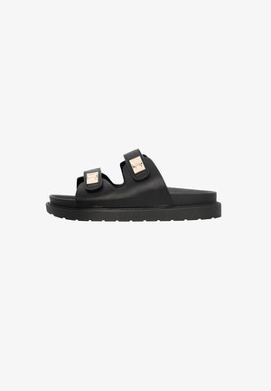 Zwarte schuifsandalen hebben twee brede straps met vierkante metalen hardware accenten, een geweven matte afwerking en een dikke rubberen zool.