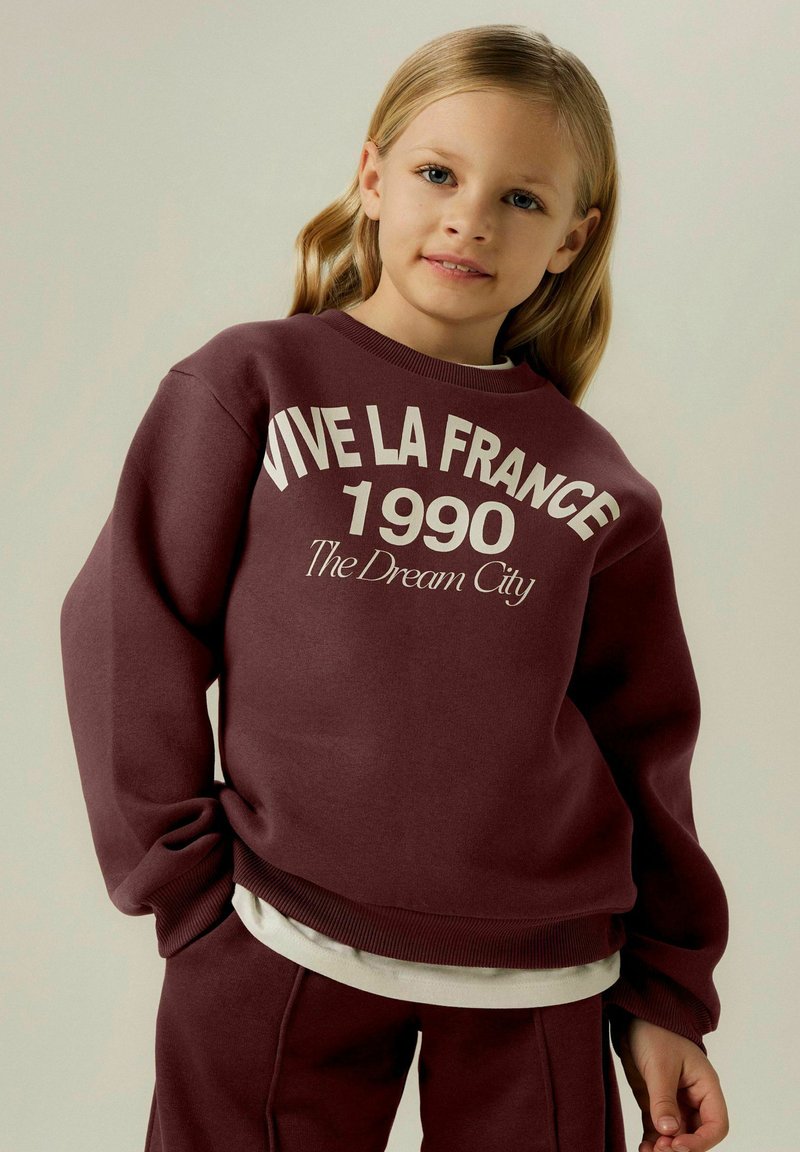 Felpa color granata con la scritta "VIVE LA FRANCE 1990 The Dream City" in crema, con polsini e orlo a coste. Abbinata a pantaloni granata coordinati.