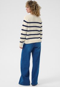 Pull rayé en crème et marine, avec des manches longues et des poignets côtelés, associé à un jean large bleu pour un style décontracté.